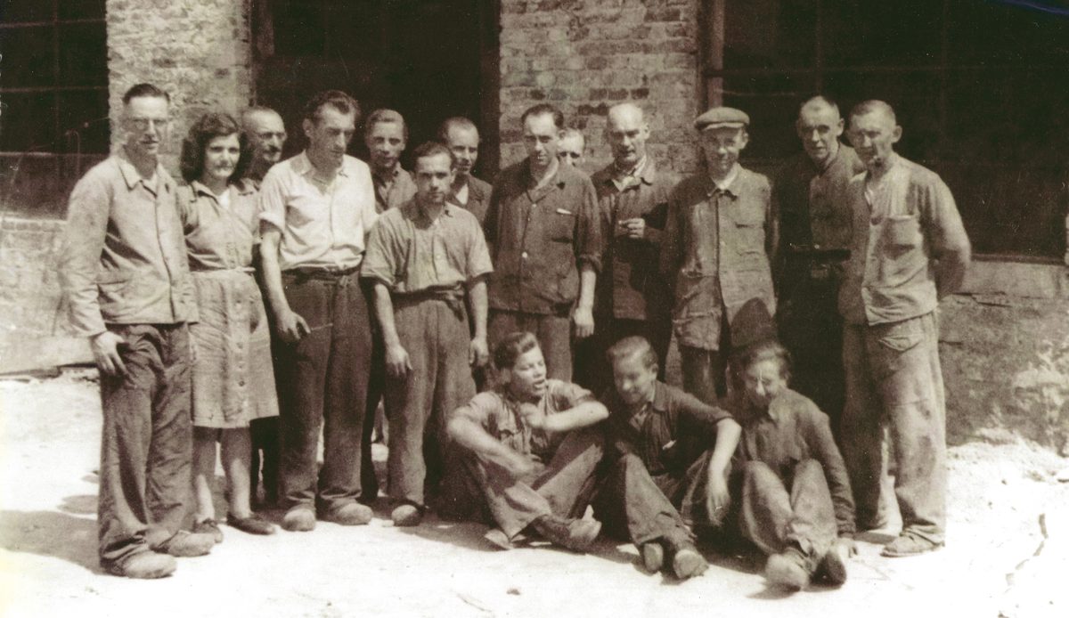 Gruppenbild der Belegschaft vor einer Backsteinwand, historische Aufnahme