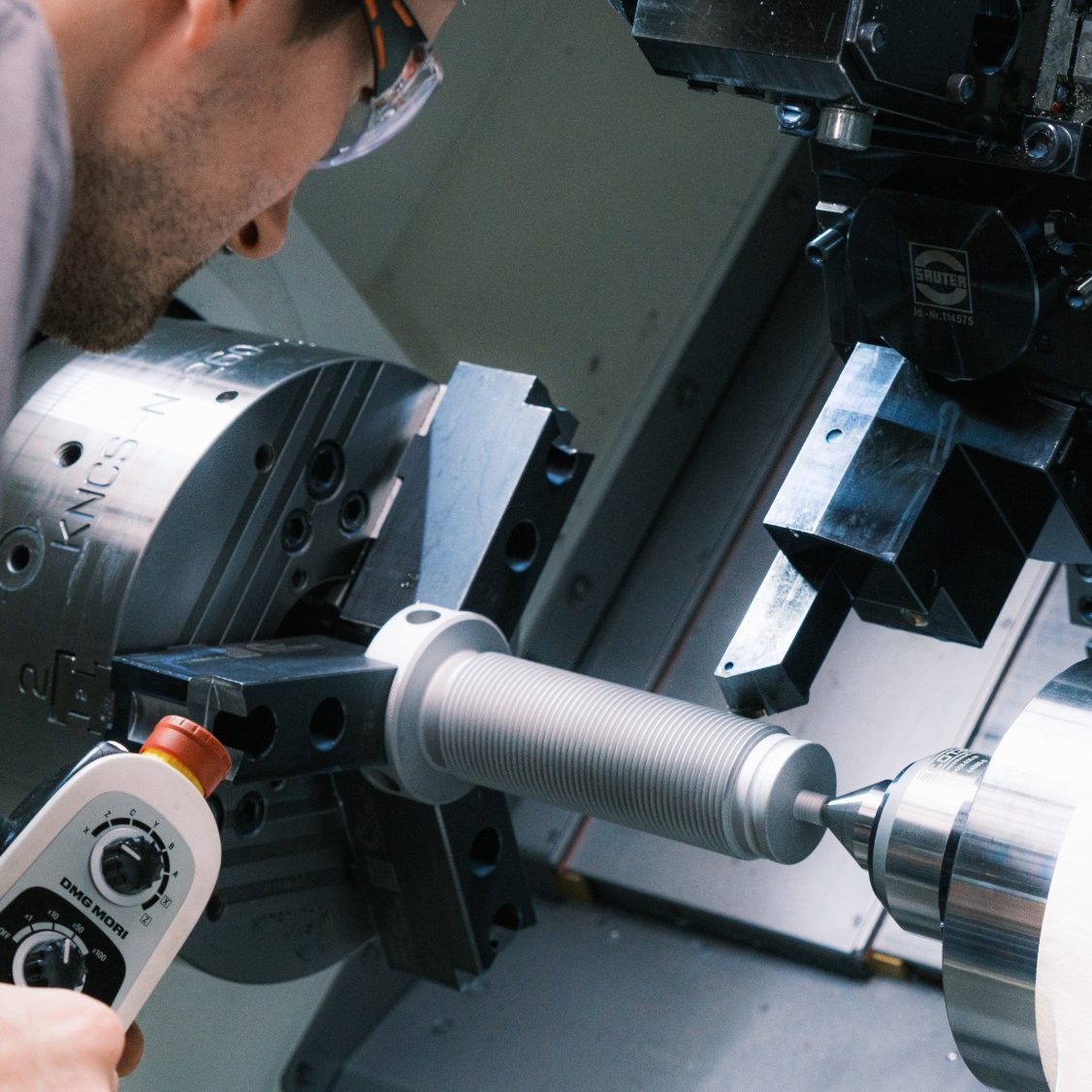 Mitarbeiter mit Schutzbrille richtet ein Gewindeteil in der Drehmaschine ein